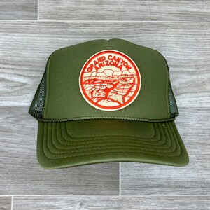 May include: A green trucker hat with a red and white embroidered patch that says "Grand Canyon Arizona".