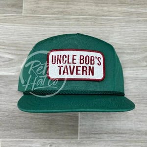 Puede incluir: Un gorro de camionero verde con un parche rojo y blanco que dice "Uncle Bob's Tavern".