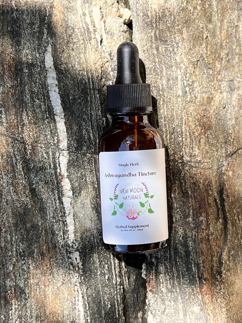 May include: A brown glass bottle with a black dropper top. The label reads "Single Herb Ashwagandha Tincture New Moon Naturals Herbal Supplement Net Wt 1 fl oz - 30ml".