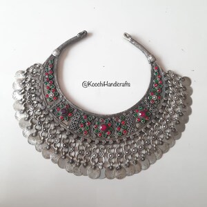 Puede incluir: Un collar de plata con forma de media luna, decorado con piedras rojas y verdes y monedas de plata colgantes. El collar es de @KoochiHandicrafts.