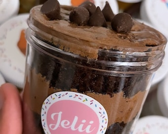 May include: A chocolate cake in a clear jar with a pink and white sticker that says "Jelli.co" and chocolate chips on top.