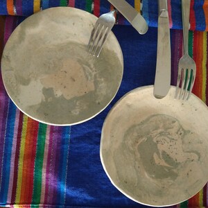 May include: Two ceramic plates with a marbled design in shades of gray and beige. The plates are on a colorful striped table runner.