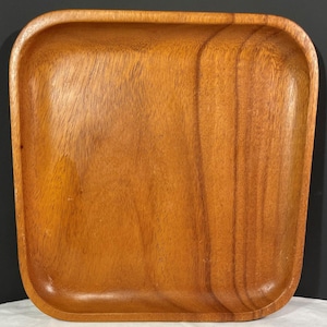 May include: Square wooden tray with rounded corners. The tray is made of a light brown wood with visible grain patterns. The tray has a slightly raised edge.