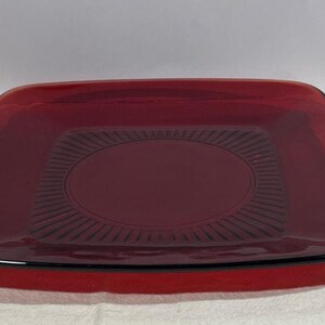 May include: A set of four pieces of ruby red glassware. The set includes a square bowl, a square plate with a circular design, a saucer, and a teacup. The glassware has a glossy finish and a modern design.