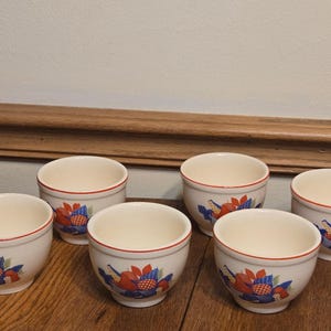 May include: Six white ceramic bowls with red, blue, and green floral designs. The bowls are arranged in two rows of three.