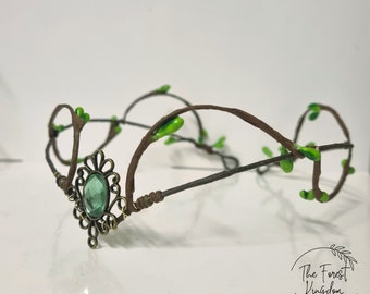 May include: A delicate crown made of brown wire with green leaves and a single green gemstone in a bronze setting.