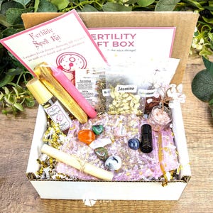 May include: A Fertility Gift Box with various items, including a roller bottle, crystals, candles, and dried herbs. The box contains a Fertility Spell Kit card and is filled with decorative paper. The box is open, revealing the contents.