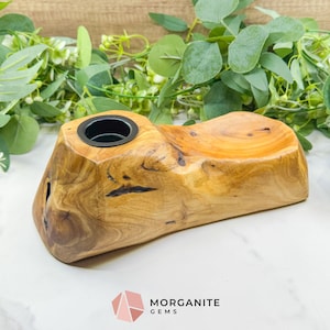 May include: A handcrafted wooden candle holder with a natural, organic shape. The holder features a single black metal cup for a candle and a smooth, curved surface. The wood grain is visible, showcasing the natural beauty of the material.