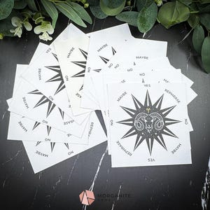 May include: A white, star-shaped, paper fortune teller with black text and a black and white illustration of a ram's head. The text on the fortune teller includes "Yes", "No", "Maybe", "Rephrase", and "On".