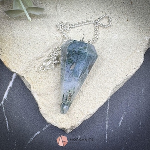 May include: A green and gray crystal pendulum on a silver chain. The pendulum is a point shape and is hanging from a silver chain.