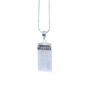 May include: A silver necklace with a rectangular, white crystal pendant. The crystal is capped with a silver metal piece and hangs from a delicate silver chain. The background is plain white.