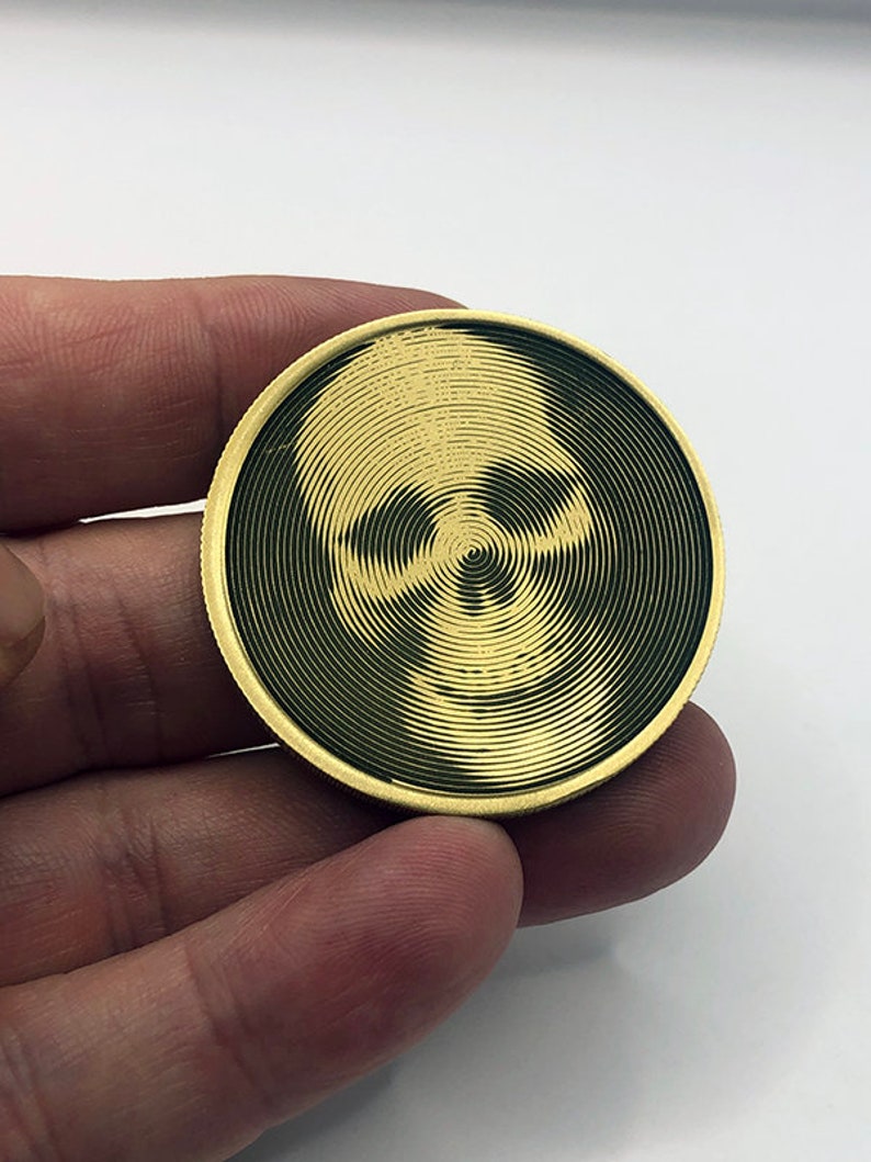 May include: A gold-colored metal coin with a black and white skull design. The skull is created using a spiral pattern.