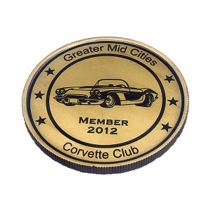 Op de afbeelding: Gouden metalen munt met een zwarte omtrek van een klassieke Corvette-auto, de tekst "Greater Mid Cities Corvette Club" en "MEMBER 2012".