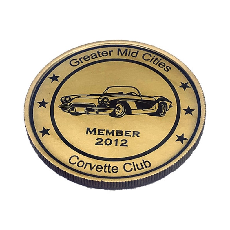 Op de afbeelding: Gouden metalen munt met een zwarte omtrek van een klassieke Corvette-auto, de tekst "Greater Mid Cities Corvette Club" en "MEMBER 2012".