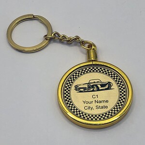 May include: Gold-colored keychain with a round, black and white checkered design. The keychain features a black silhouette of a classic car and the text "C1 Your Name City, State".