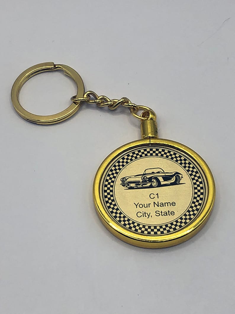 May include: Gold-colored keychain with a round, black and white checkered design. The keychain features a black silhouette of a classic car and the text "C1 Your Name City, State".