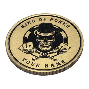 May include: Gold-colored coin with a black and white design of a skull wearing a fedora hat and holding playing cards. The text "KING OF POKER" and "YOUR NAME" are printed around the design.