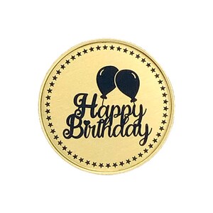 May include: A gold round coin with a black border of stars. The center of the coin has the text "Happy Birthday" in a black cursive font with two black balloons above the text.