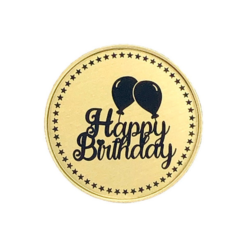 May include: A gold round coin with a black border of stars. The center of the coin has the text "Happy Birthday" in a black cursive font with two black balloons above the text.