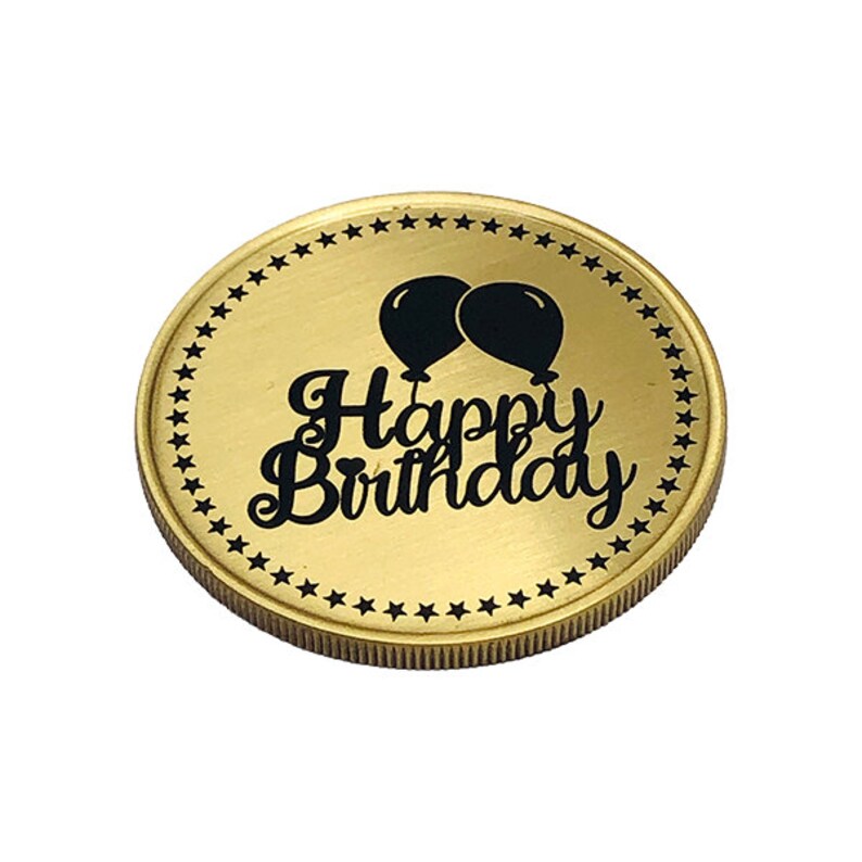May include: A gold-colored coin with a black inscription that reads "Happy Birthday" and two black balloons. The coin is surrounded by a border of black stars.