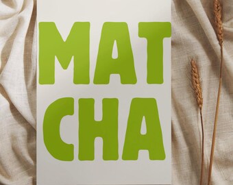 May include: A white rectangular print with the word "MATCHA" in large, bright green letters. The print is set against a neutral-toned, textured fabric background, with two stalks of wheat on the right side.