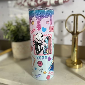 Puede incluir: Un vaso de acero inoxidable azul claro con un dise&ntilde;o de purpurina rosa, azul y morado. El vaso presenta un gr&aacute;fico de Jack Skellington y Sally de la pel&iacute;cula Pesadilla antes de Navidad. El gr&aacute;fico incluye las palabras "love", "xoxo" y "love" en una fuente rosa, azul y morada.