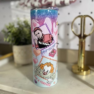 Puede incluir: Un vaso de glitter rosa y azul con fondo blanco. El vaso presenta un gr&aacute;fico de un personaje de la pel&iacute;cula "It" y un personaje de la pel&iacute;cula "Halloween". El texto "Now & Forever" est&aacute; impreso en el vaso.