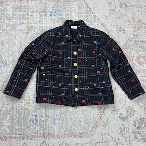 May include: A black long-sleeve jacket featuring a grid pattern of thin white lines and small, colorful square accents in red, blue, green, and yellow. The jacket has a pointed collar, long sleeves, and a front button closure with four yellow buttons.