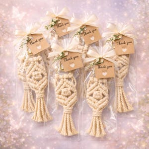 Pu&ograve; includere: Diversi portachiavi in macram&egrave; beige in sacchetti di plastica trasparente, legati con fiocchi color crema e piccoli accenti floreali. Ogni portachiavi ha un piccolo tag con la scritta "Thank you" con un cuore. I portachiavi hanno un nappa in basso.