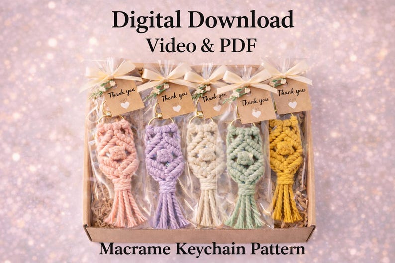 Pu&ograve; includere: Una collezione di cinque portachiavi in macram&egrave; in una scatola, ognuno in un colore pastello diverso: pesca, lavanda, crema, verde menta e giallo. Ogni portachiavi &egrave; adornato con un anello color oro e un piccolo tag con la scritta "Thank you". &Egrave; visibile anche il testo "Download digitale Video e PDF" e "Modello portachiavi macram&egrave;".