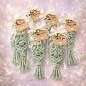 Pu&ograve; includere: Portachiavi in macram&egrave; verde salvia, confezionati singolarmente in cellophane trasparente. Ogni portachiavi &egrave; adornato con un fiocco color crema, un piccolo rametto di fiori e un'etichetta con la scritta "Thank you."