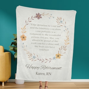 Puede incluir: Una manta de forro polar blanca con un borde de corona floral y el texto "Tu dedicación a tu trabajo y la amabilidad que muestras a tus pacientes es un testimonio de la persona maravillosa que eres. Que siempre estés orgulloso del trabajo que has hecho y de las vidas que has tocado." El texto "Feliz Jubilación Karen, RN" está debajo de la corona.