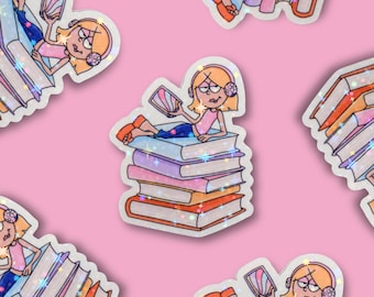 May include: Sticker sheet featuring a cartoon illustration of a girl with orange hair wearing headphones, reading a tablet while lounging on a stack of books. The stickers have a holographic glitter effect and are set against a pink background.