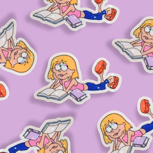 May include: A repeating pattern of stickers featuring a cartoon girl with blonde hair, glasses, and a pink top, reading a book. The girl is lying down, with a book open in front of her and a smaller book beside her. The stickers have a glittery effect.