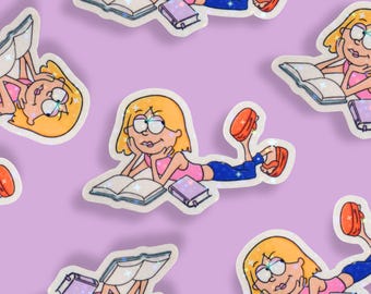 May include: A repeating pattern of stickers featuring a cartoon girl with blonde hair, glasses, and a pink top, reading a book. The girl is lying down, with a book open in front of her and a smaller book beside her. The stickers have a glittery effect.