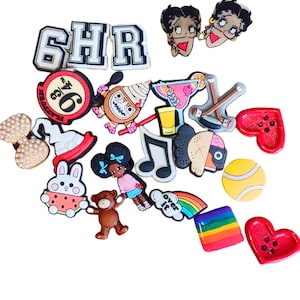 Op de afbeelding: Een verzameling kleurrijke schoenbedels met verschillende ontwerpen, waaronder cartoonfiguren, muzieknoten, harten, een regenboog en een watermeloen. De bedels zijn gemaakt van rubber en hebben een glanzende afwerking.