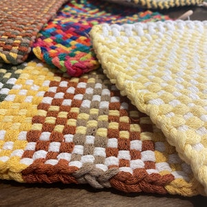 May include: A set of five woven pot holders in various colors and patterns, including brown, yellow, white, red, and blue. The pot holders are made of a thick, woven material and are designed to protect surfaces from heat.