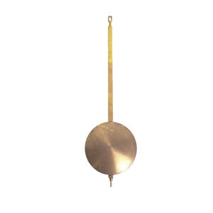 May include: A vintage brass clock pendulum with a circular weight and a long, rectangular rod. The pendulum has a small, pointed tip at the bottom of the weight and a loop at the top. The brass has a warm, aged patina.