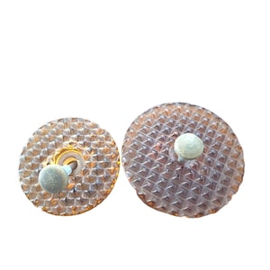 May include: Two amber-colored bottle stoppers with a textured, diamond-like pattern. Each stopper has a small, round, light green knob on top. The stoppers are round and appear to be made of glass or a similar material.