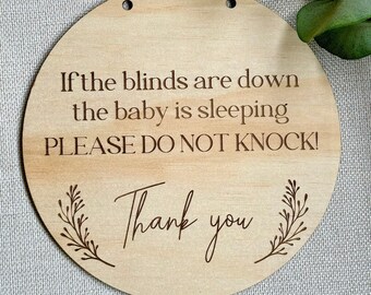 May include: A round wooden sign with the text "If the blinds are down the baby is sleeping PLEASE DO NOT KNOCK! Thank you" engraved on it. The sign has two holes at the top for hanging.