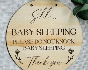 May include: A round wooden sign with the text "Shh... Baby Sleeping Please Do Not Knock. Baby Sleeping Thank You" in a cursive font. The sign has two holes at the top for hanging.