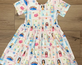 May include: A white short-sleeved dress with a colorful pattern featuring cartoon characters, castles, and other fairytale elements. The dress has a round neckline and a gathered skirt, perfect for a young girl.