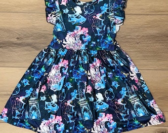 May include: A dark blue dress with a whimsical Alice in Wonderland print. The dress features a round neckline, flutter sleeves, and a flared skirt. The print includes Alice, clocks, teacups, and the text "WE'RE ALL MAD HERE".