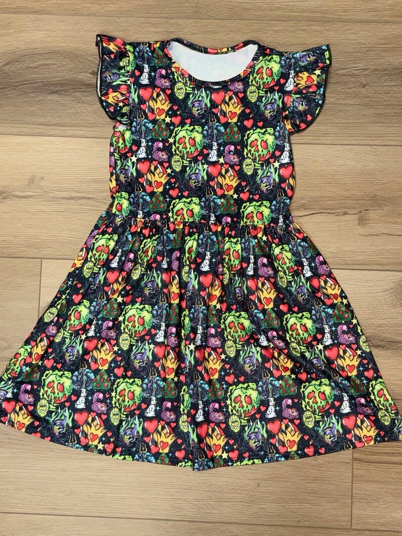May include: A black dress with a colorful pattern featuring green poison apples, red hearts, and other whimsical designs. The dress has short sleeves and a gathered waist, creating a flared skirt. The fabric has a white neckline.
