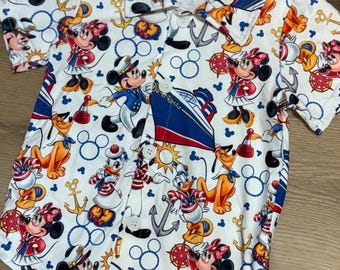 May include: White button-up shirt with a nautical-themed print featuring Mickey and Minnie Mouse, Donald Duck, Pluto, anchors, and ships. The collar and sleeve trim have red and blue stripes. The shirt has short sleeves and white buttons.