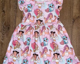 May include: A pink and blue patterned dress featuring a repeating design of cartoon characters and blue cats. The dress has a round neckline and ruffled sleeves. The fabric has a gradient effect, transitioning from pink to blue.