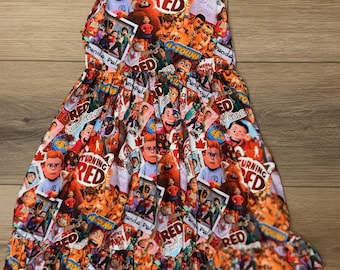 May include: A sleeveless dress featuring a colorful print with characters and text from the movie "Turning Red." The design includes images of the characters, the words "Turning Red," and "Panda Pals" in a vibrant, eye-catching pattern. The dress has a ruffled hem.