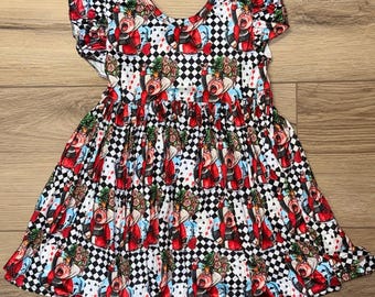 May include: A sleeveless dress with a black and white checkered pattern and a repeating print of a cartoon queen in red, white, and black. The dress has ruffled sleeves and a gathered waist.