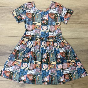 May include: A short-sleeved dress featuring a colorful, patterned design. The dress has a scoop neckline and a gathered skirt. The pattern is composed of various cartoon-like illustrations in a patchwork style, with a mix of blues, pinks, and oranges.