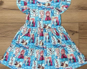 May include: A light blue dress with a pattern featuring characters from a popular animated film. The dress has short, ruffled sleeves and a flared skirt. The pattern includes images of characters, snowflakes, and the text "LET IT GO".
